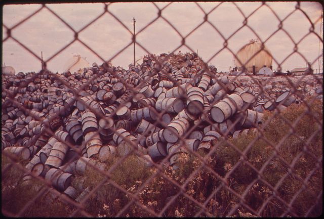 1280px-A_MOUNTAIN_OF_DAMAGED_OIL_DRUMS_NEAR_THE_EXXON_REFINERY_-_NARA_-_546004