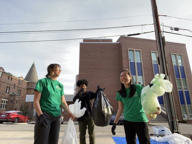 Young adults smiling while holding clear and opaque garbage bags
