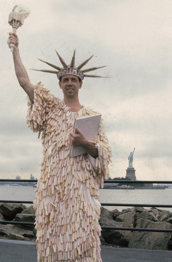 person in a statue of liberty costume made of tampon applicators posing in New York City, with the statue of liberty visible behind them