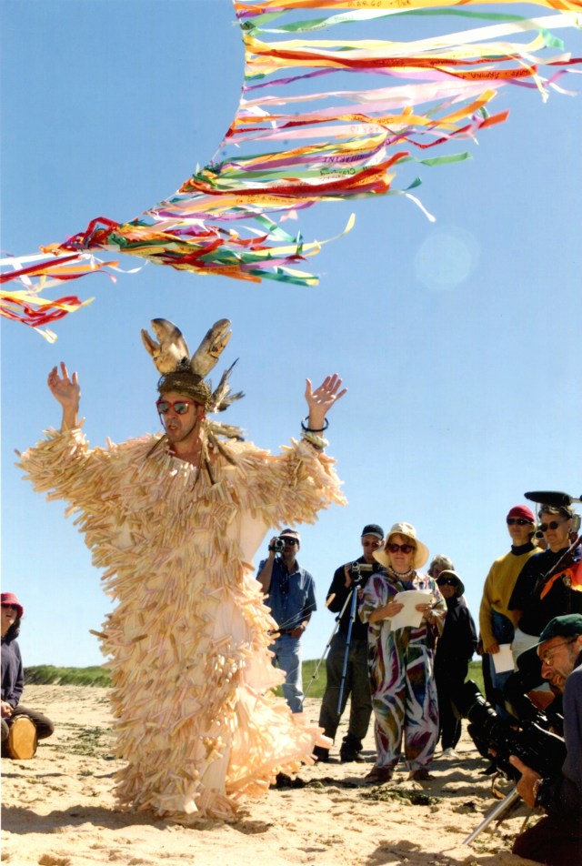 A person in a white statue of liberty costume raises hands under a colourful banner